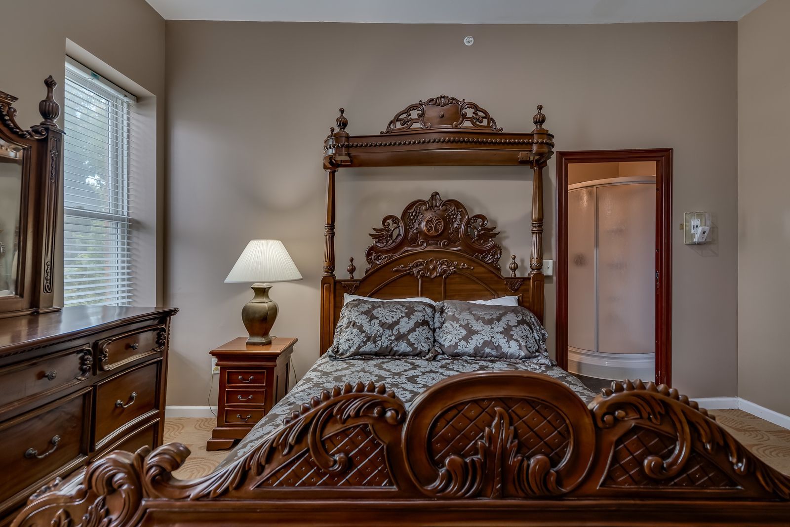 A bedroom with a canopy bed , nightstand , mirror and dresser.