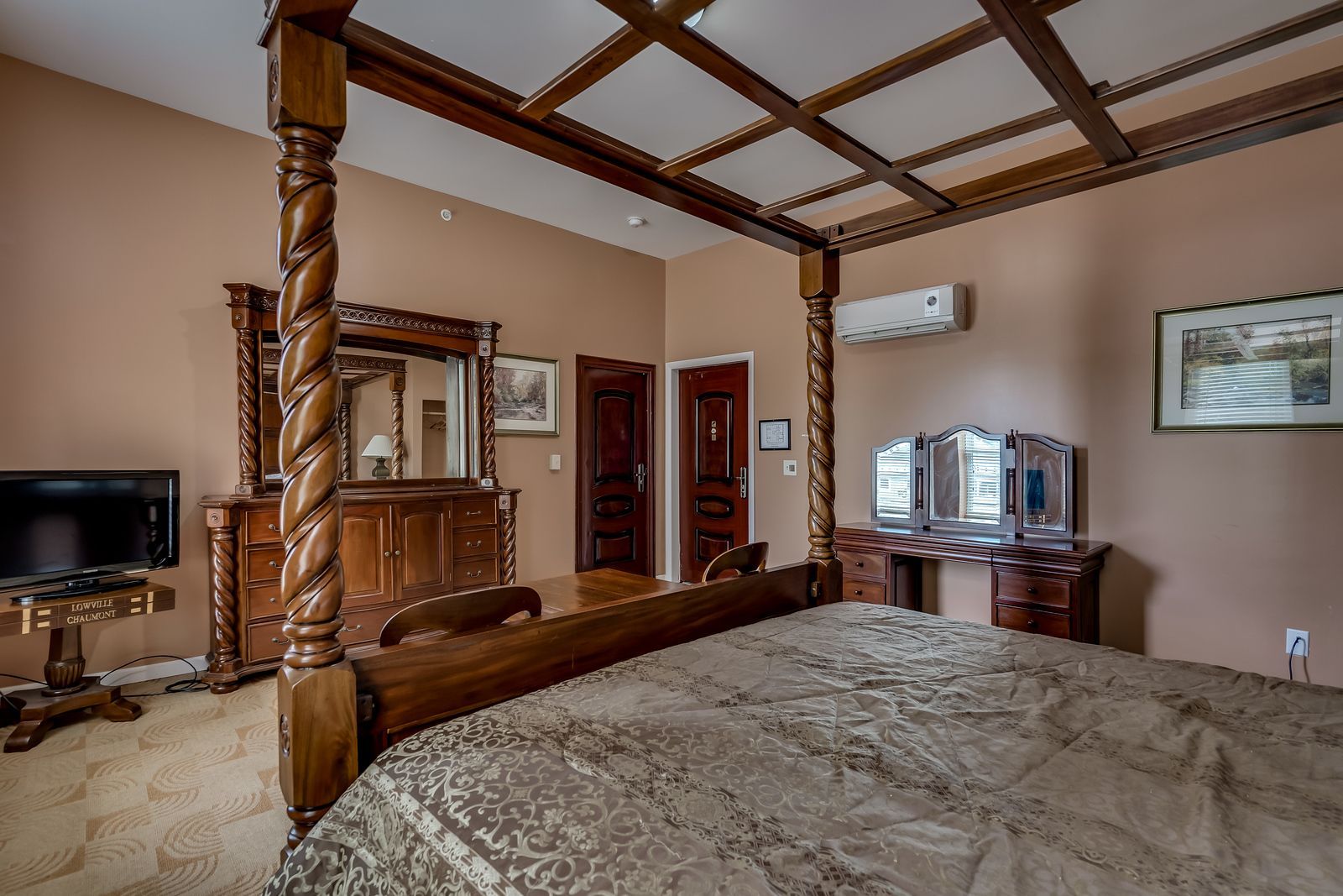 A bedroom with a four poster bed , dresser , mirror and television.
