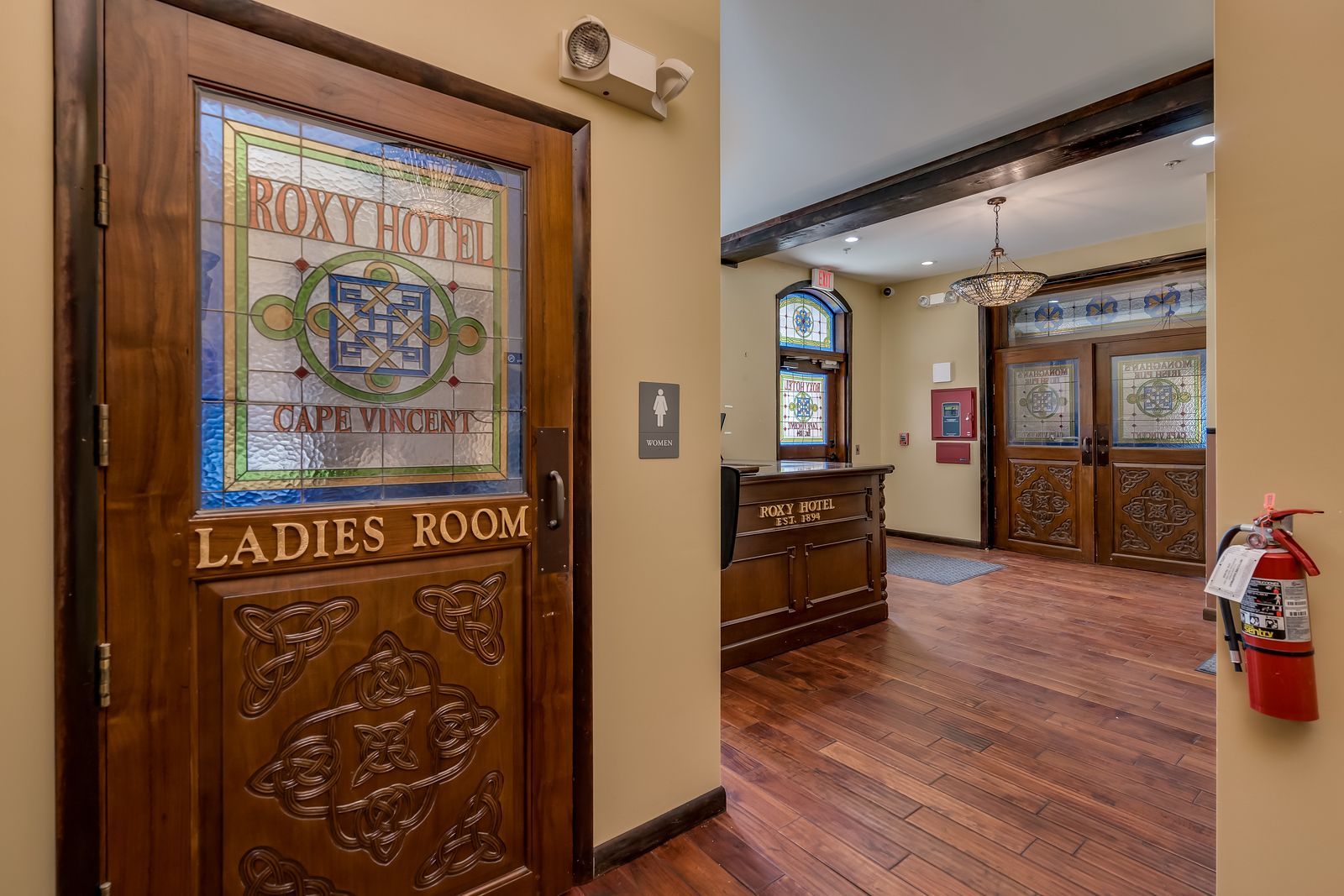 A wooden door with a stained glass window leading to a ladies room.