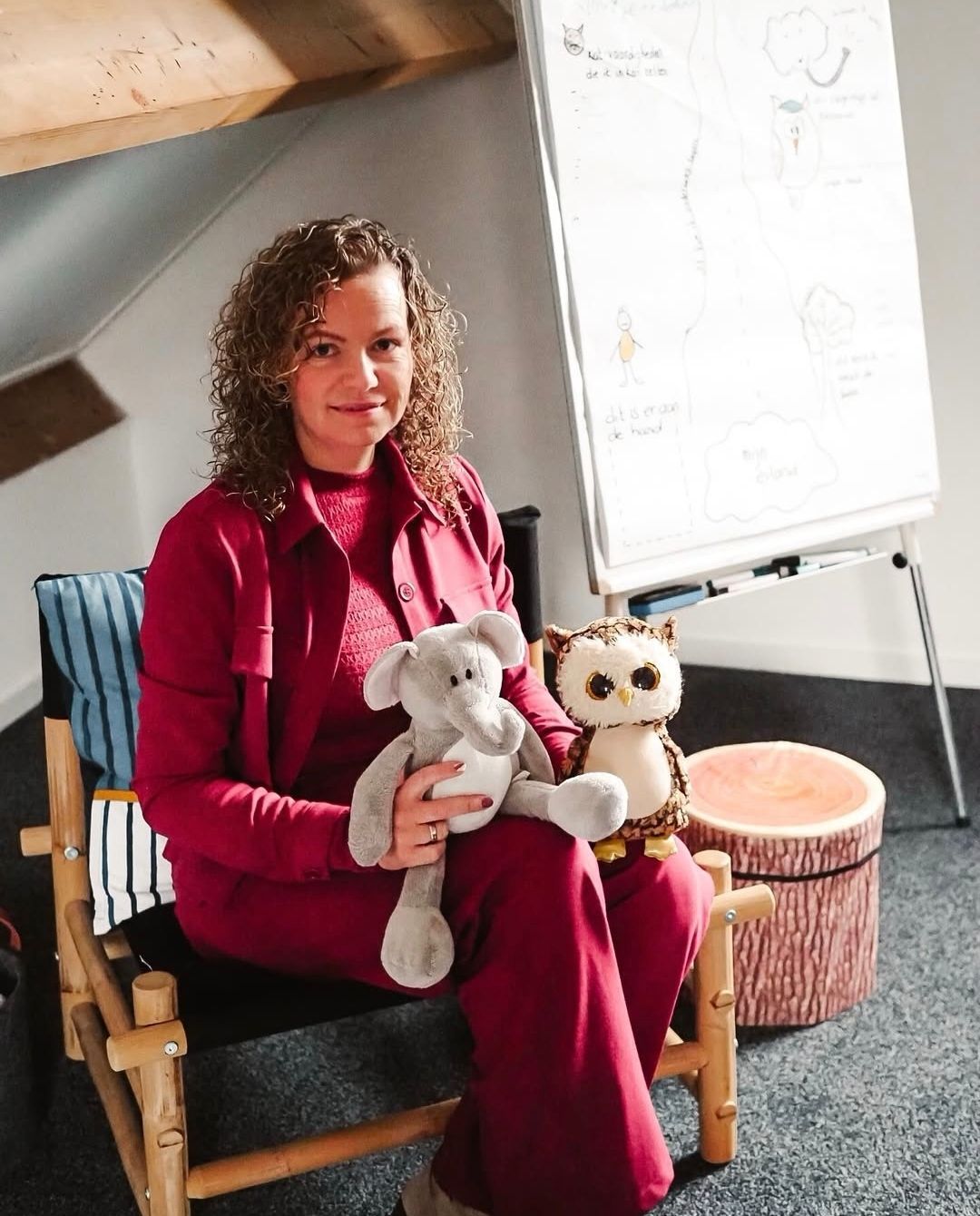 Een vrouw zit op een stoel met een teddybeer en een uil in haar armen.