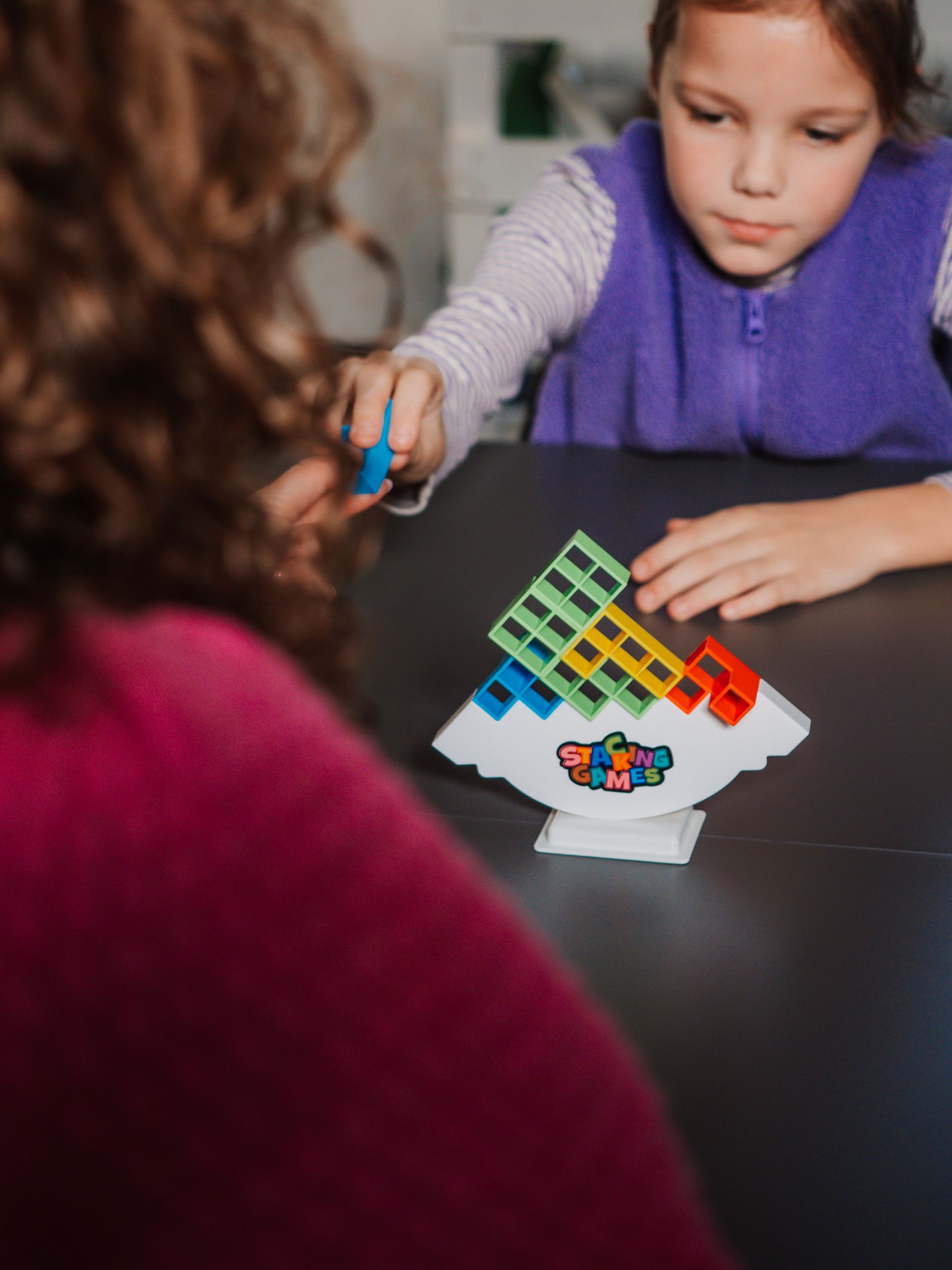 Een klein meisje speelt een spel met een vrouw aan een tafel.