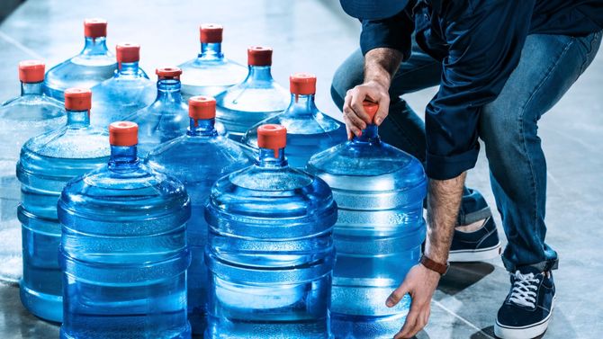 Person stacking large blue water jugs in a storage area - Indian Peaks Spring Water