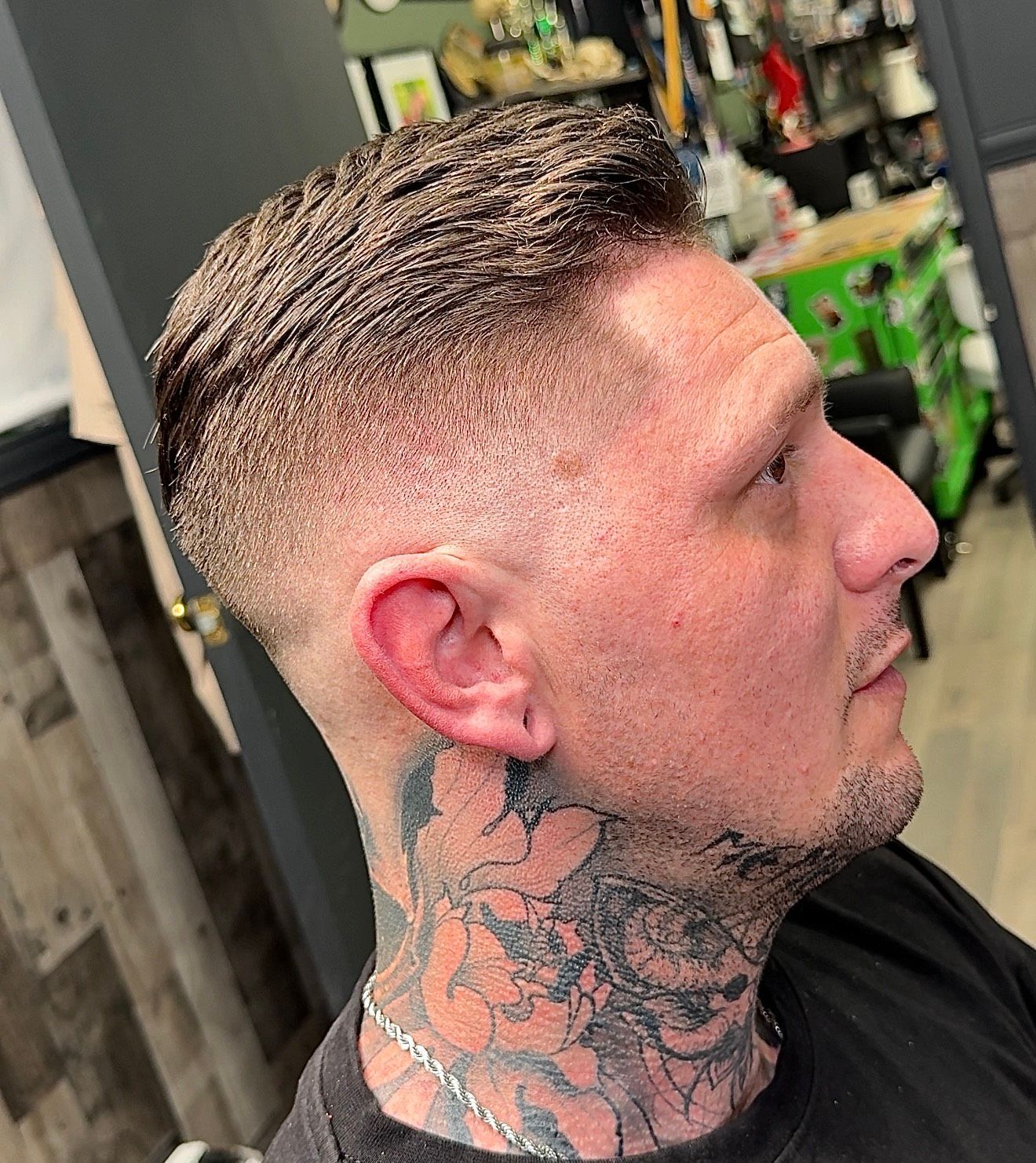 Man with a faded haircut, neck tattoos, and a contemplative expression. Inside a shop.