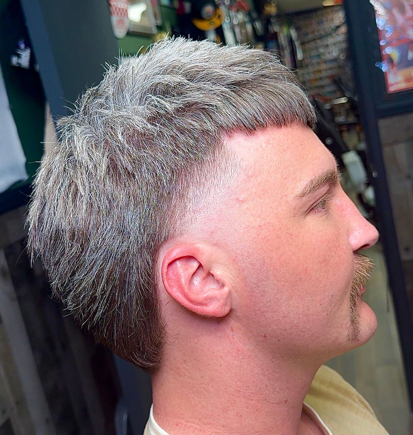 Man with a faded haircut, graying hair, and a handlebar mustache; profile view.