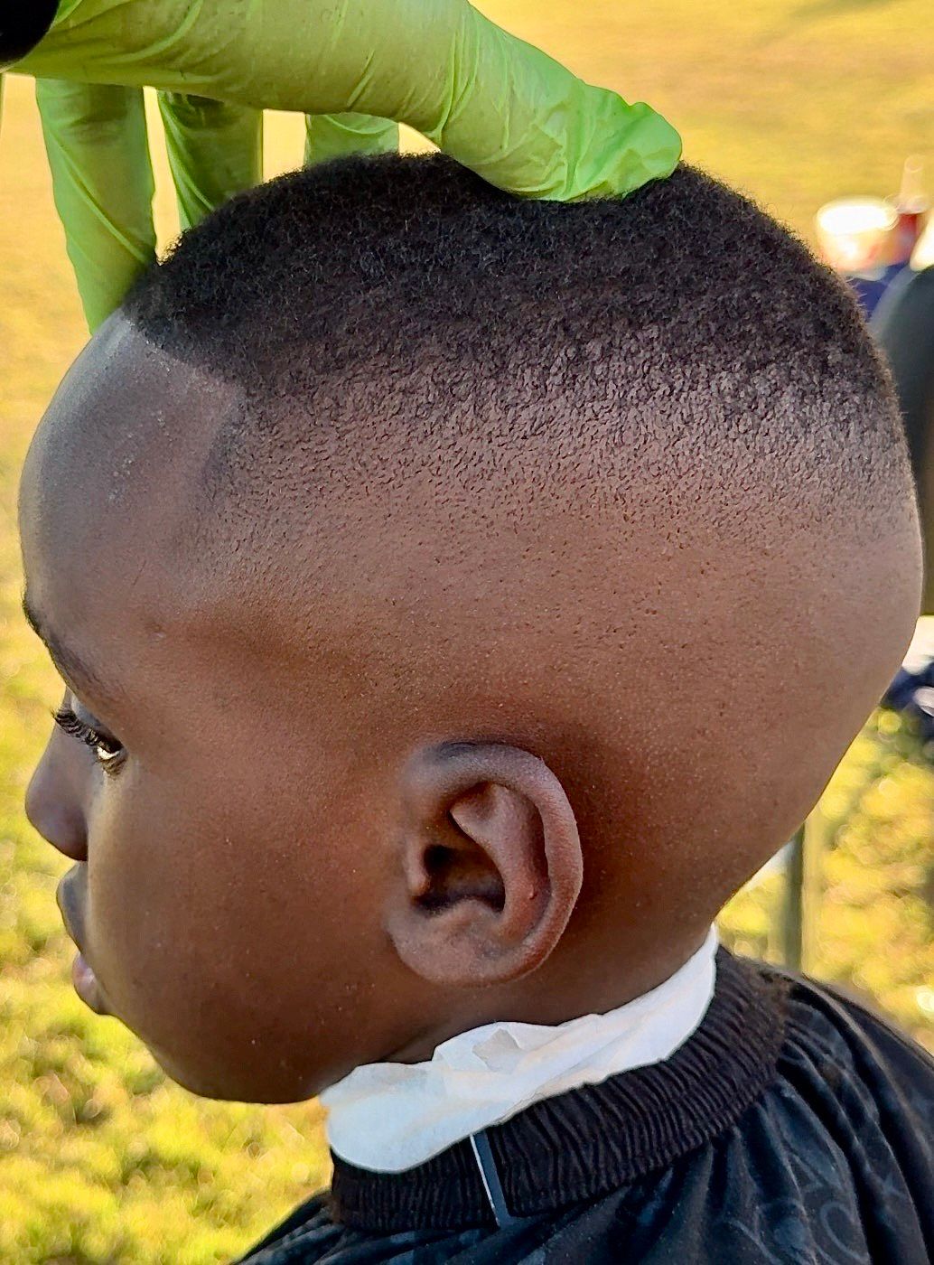 Close-up of a person's head with a haircut; the skin fades from dark to light; a green-gloved hand touches the head.