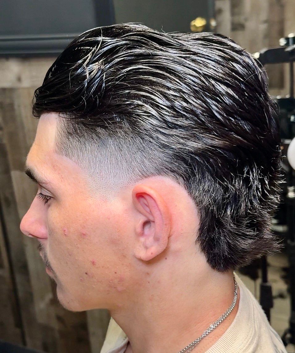 Man with a dark, slicked-back mullet hairstyle; faded sides.