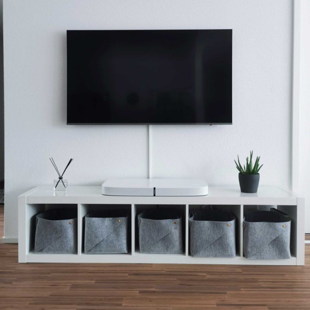 A flat screen tv is mounted on a wall above a shelf with baskets