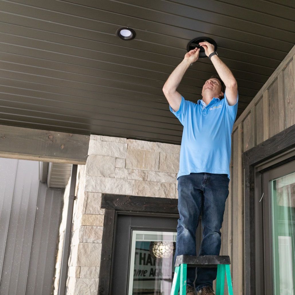 A man in a blue shirt is standing on a ladder fixing a light