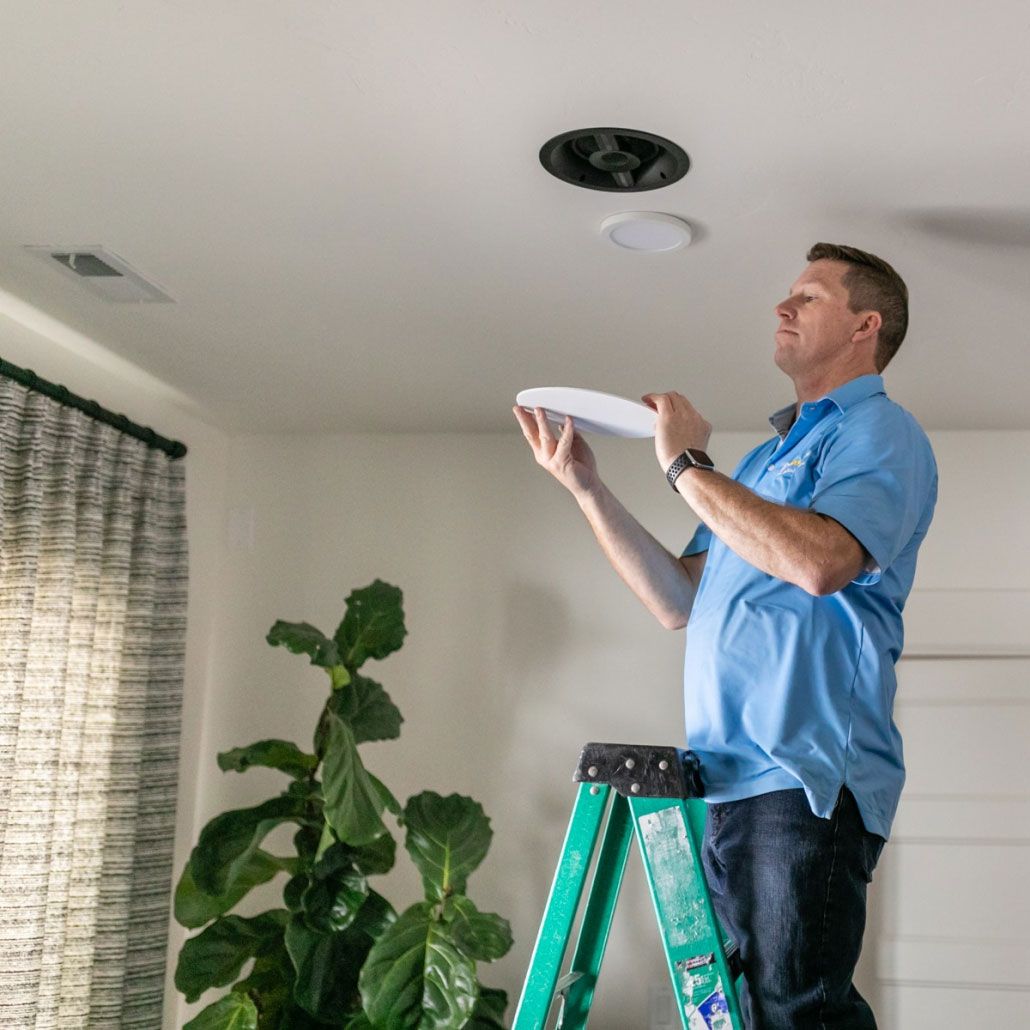 A man is standing on a ladder in a living room holding a plate