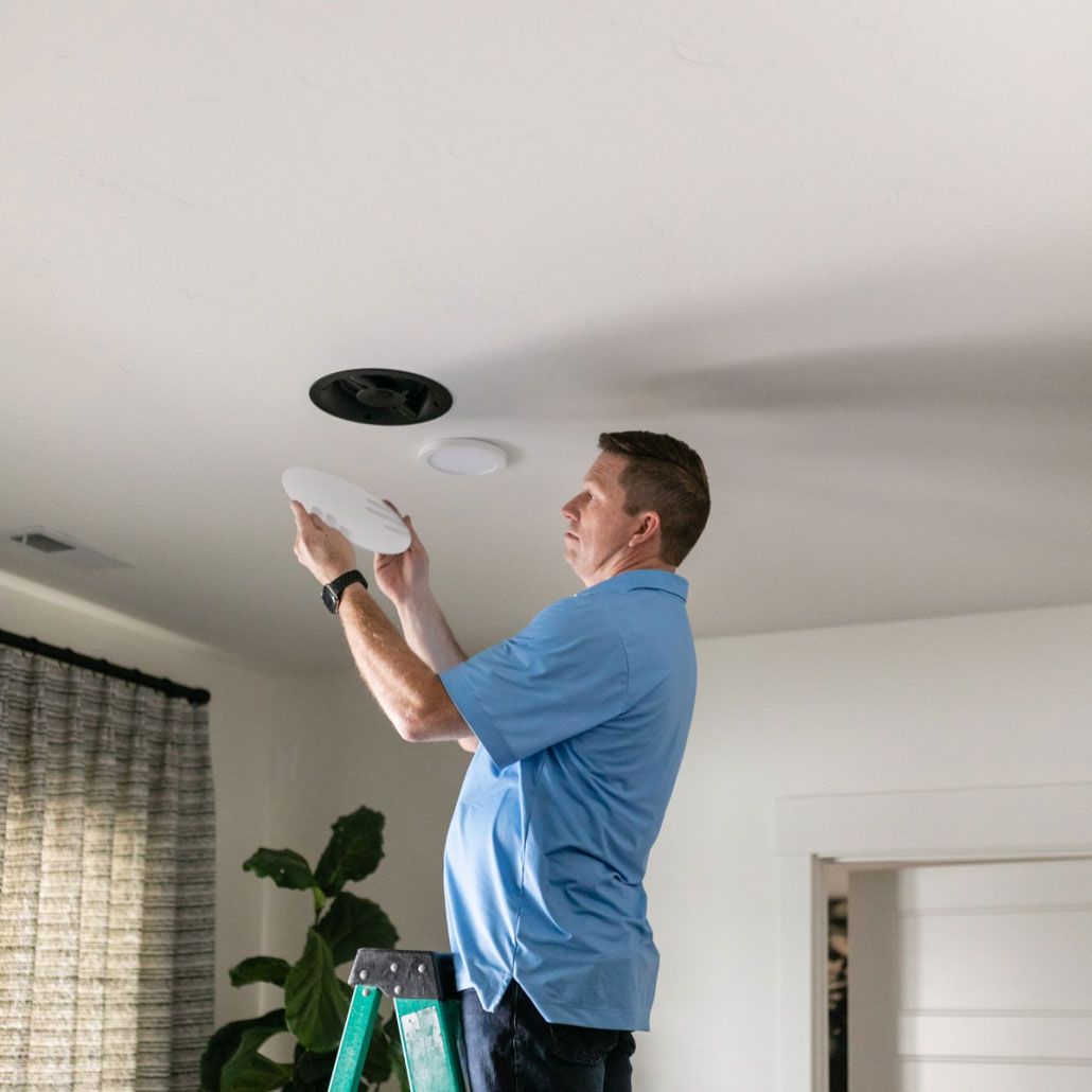 A man is standing on a ladder fixing a light fixture on the ceiling