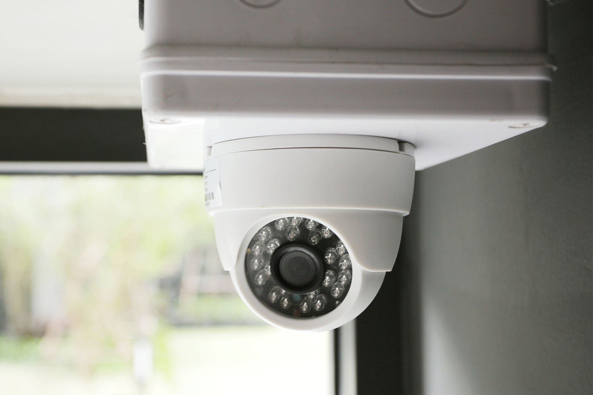 A security camera is hanging from the ceiling next to a window