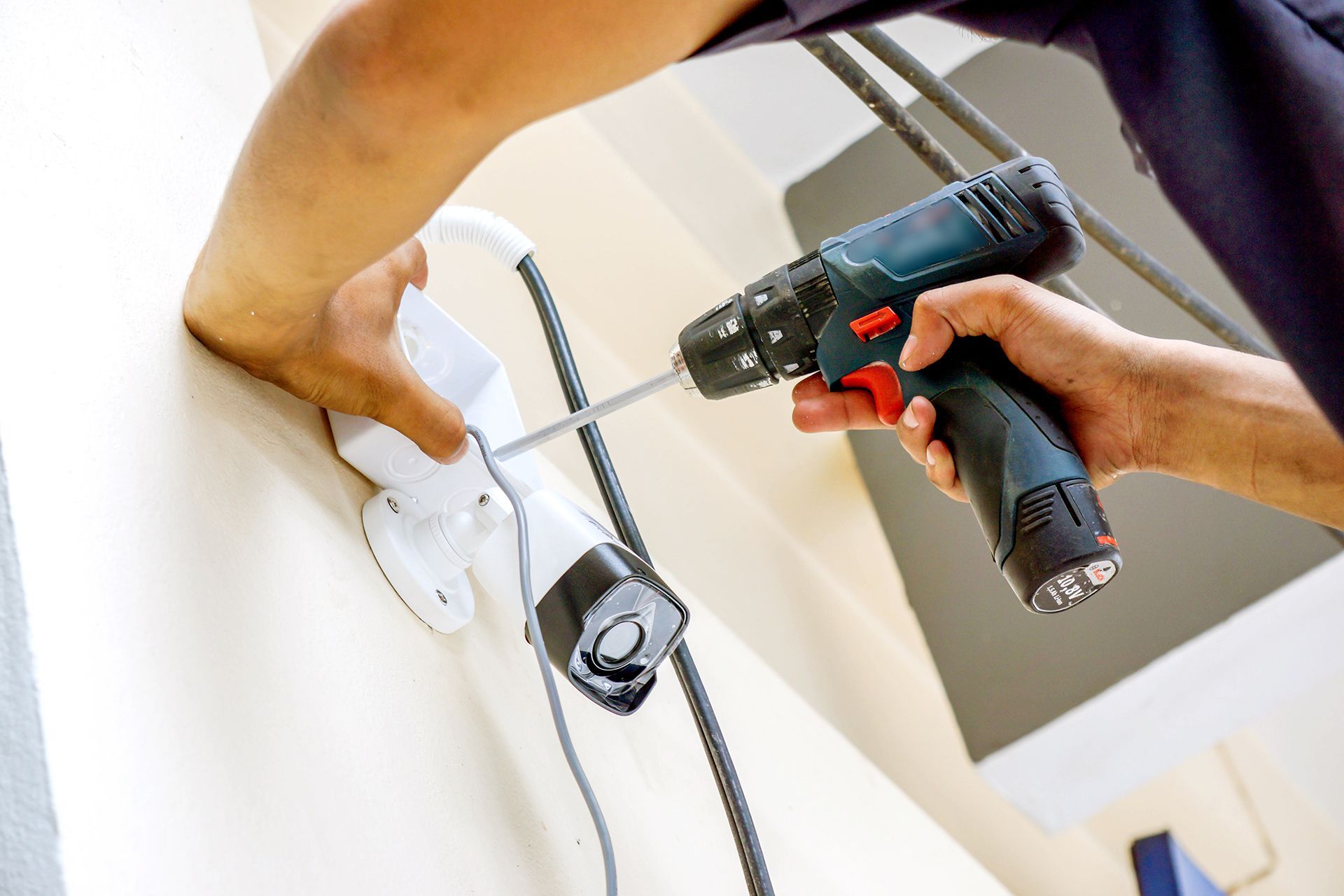 A man is using a drill to install a security camera on a wall