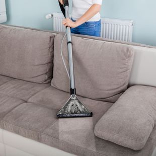 a woman is cleaning a couch with a vacuum cleaner