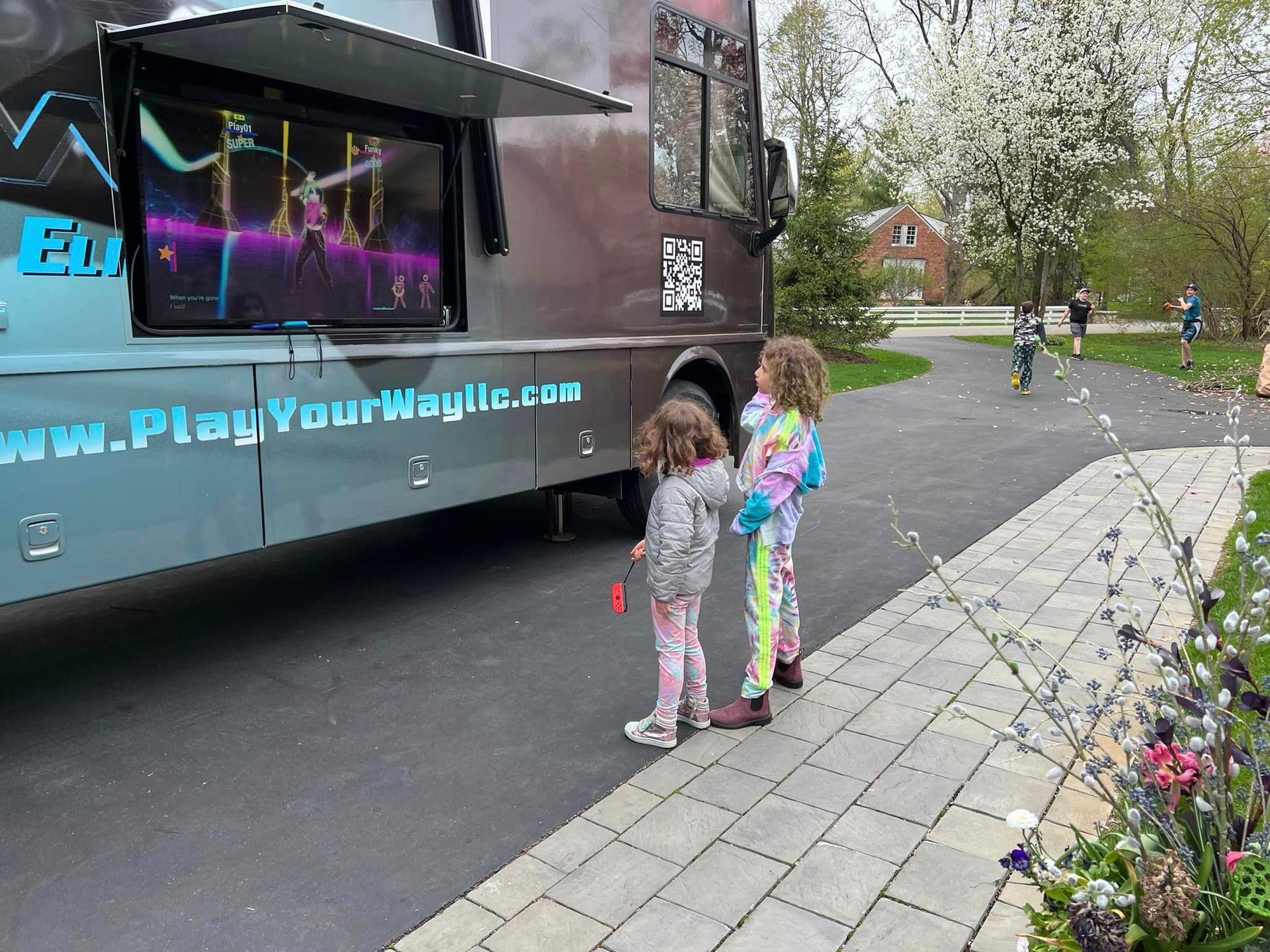 two little girls are standing in front of a play your way bus