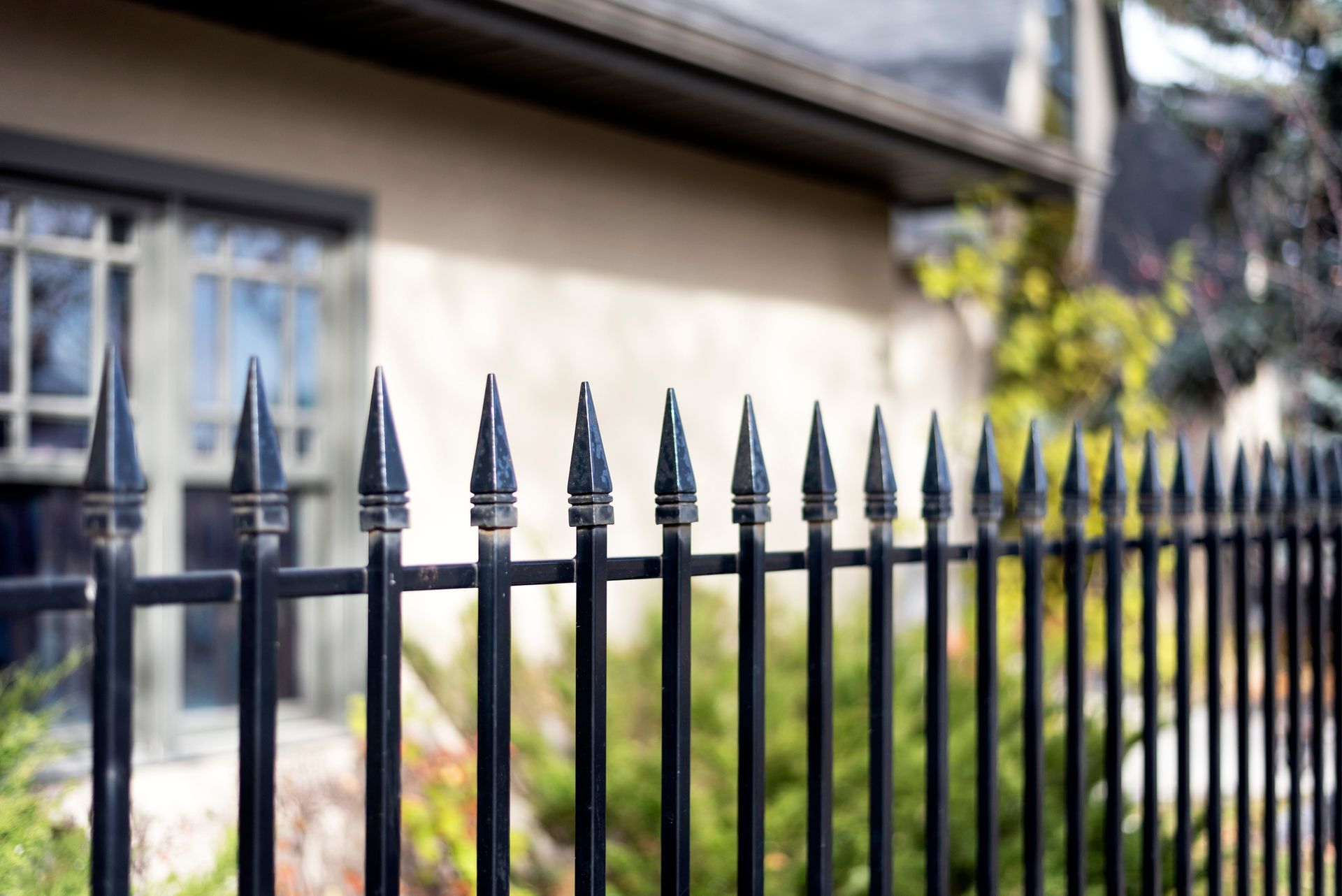 Gray horizontal slat fence on a white wall with greenery in front.