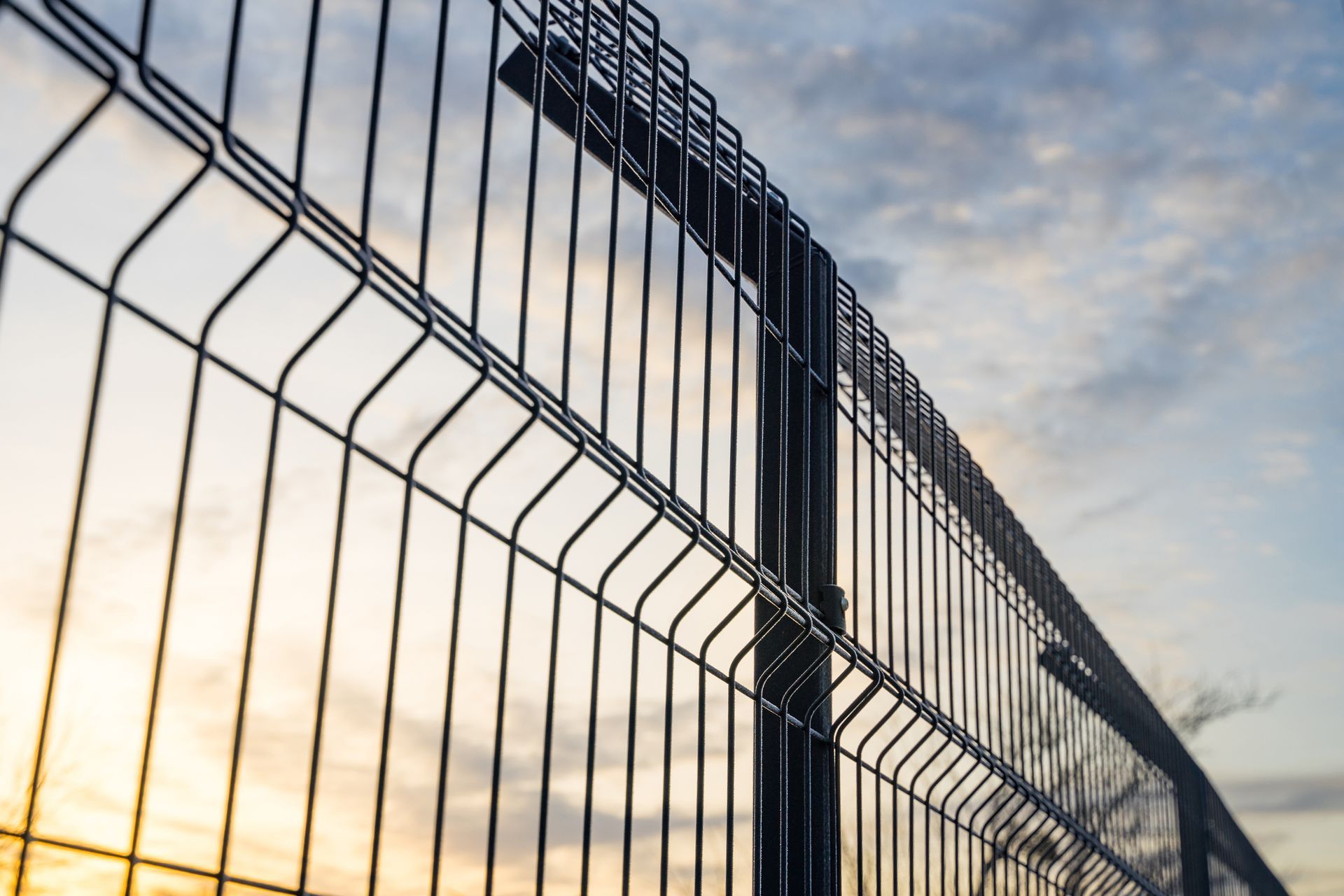 Black wire mesh fence against a cloudy sky at sunset.