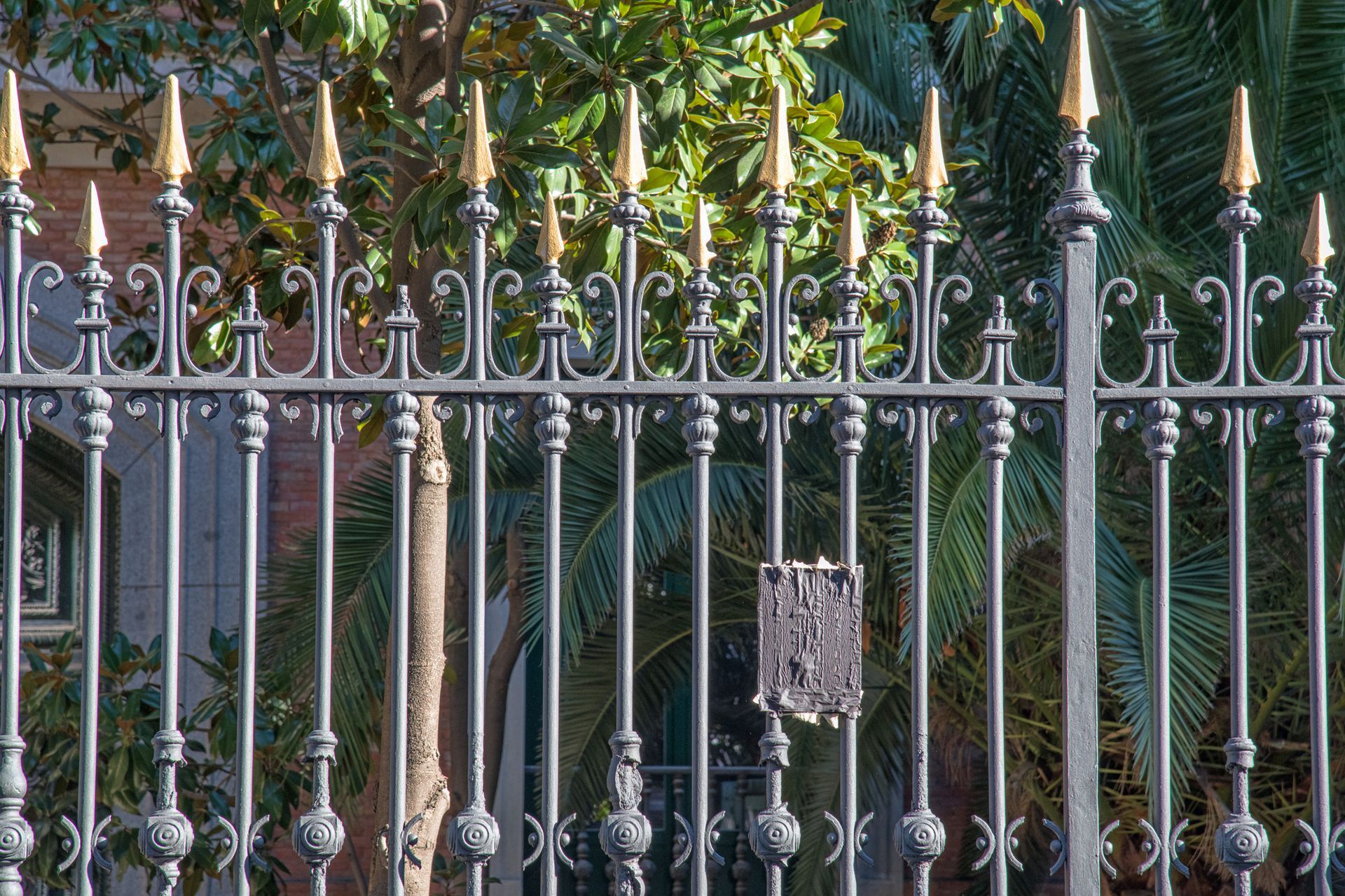 Black wrought iron fence with gold-tipped spear finials, in front of trees.