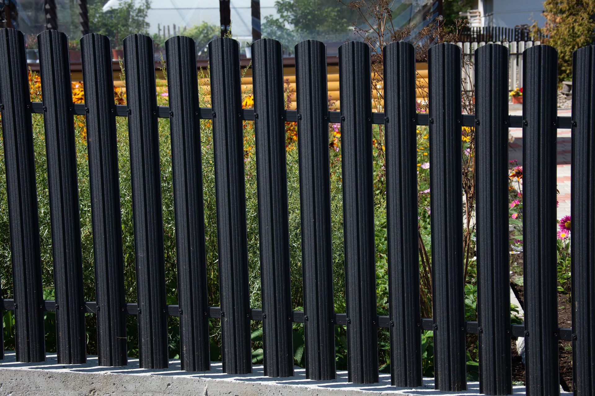 Black vertical fence with rounded posts, in front of greenery.