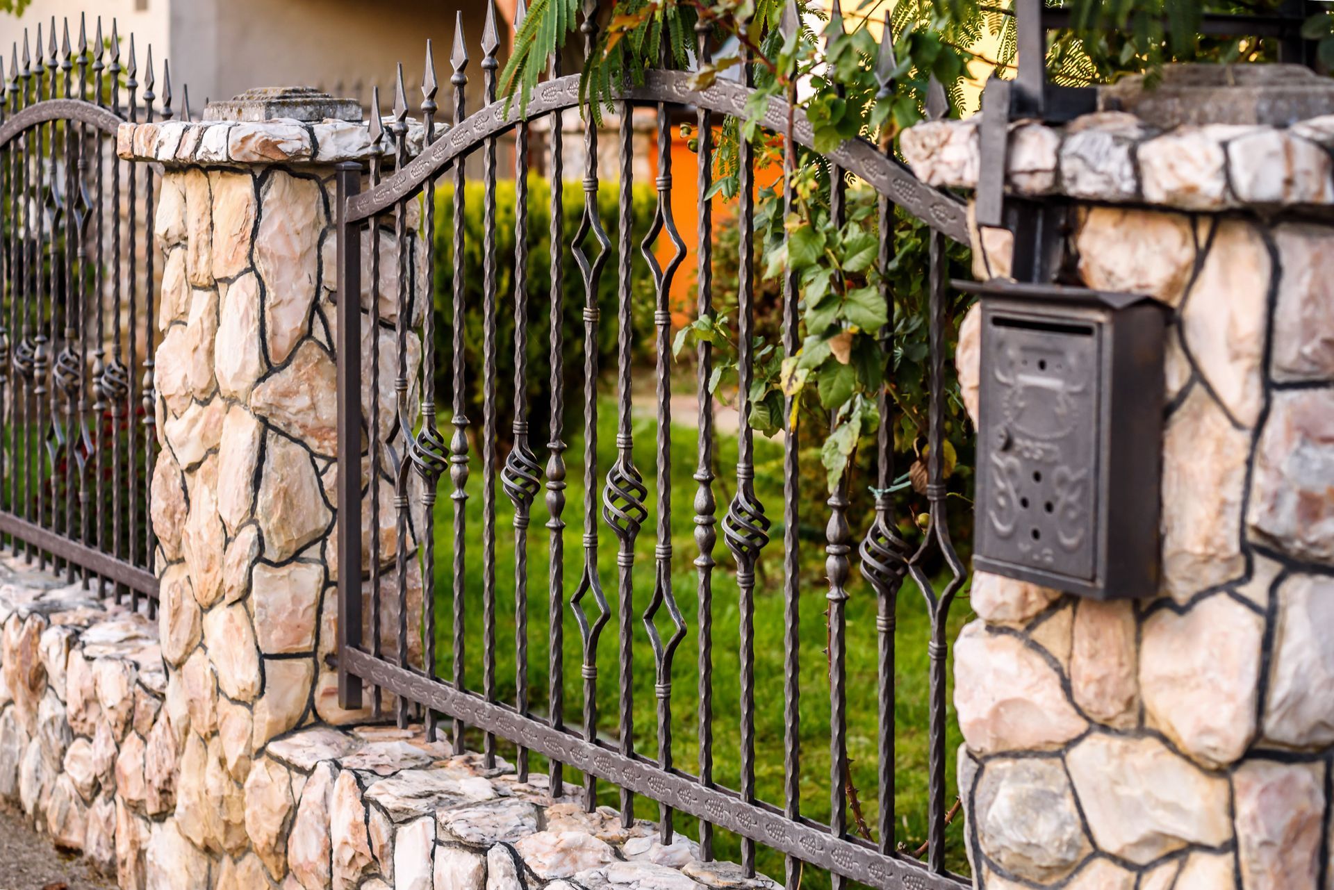 Stone fence with black metal bars and a mailbox.