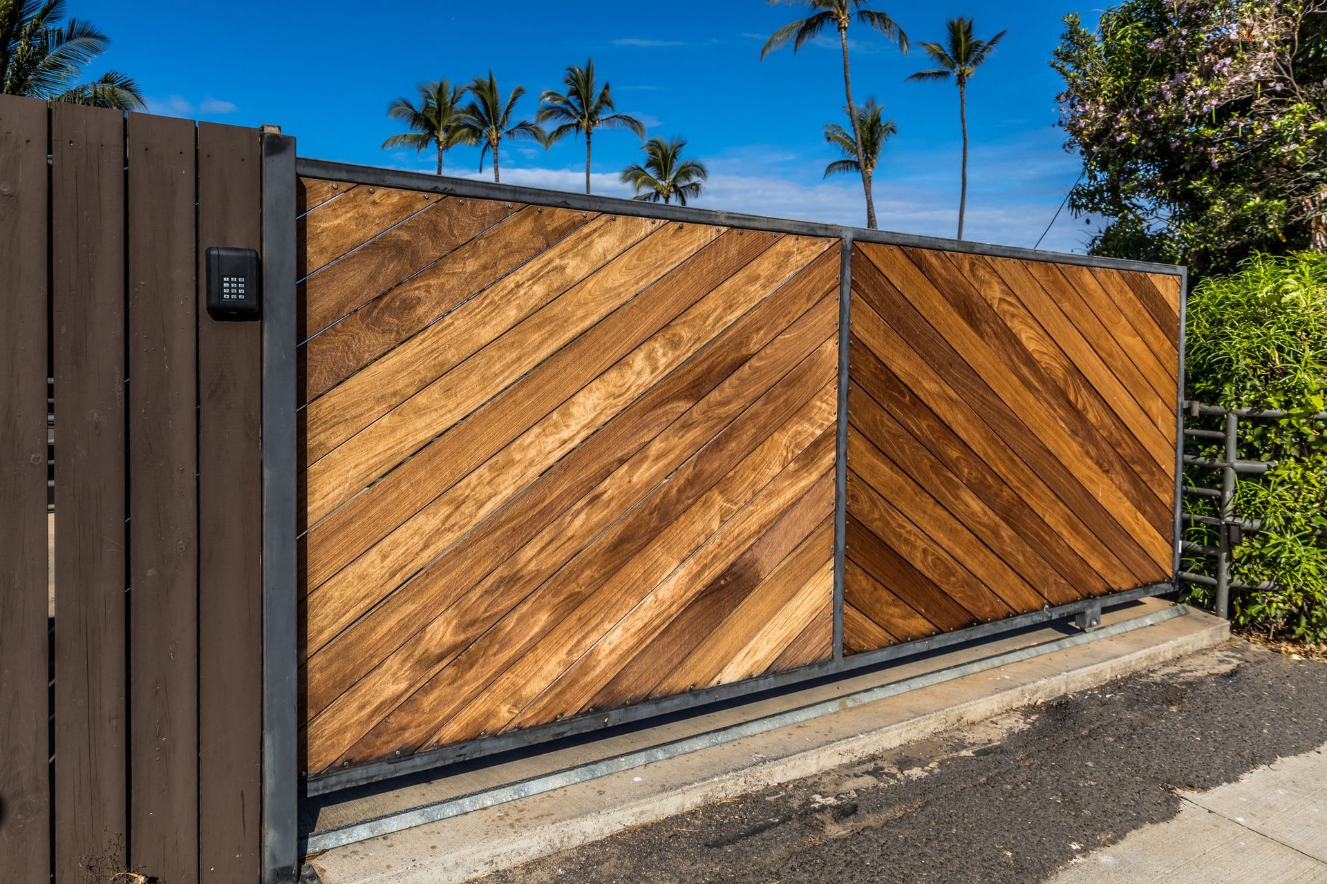 Wooden gate with diagonal planks, set in dark frame. Palm trees and blue sky background.