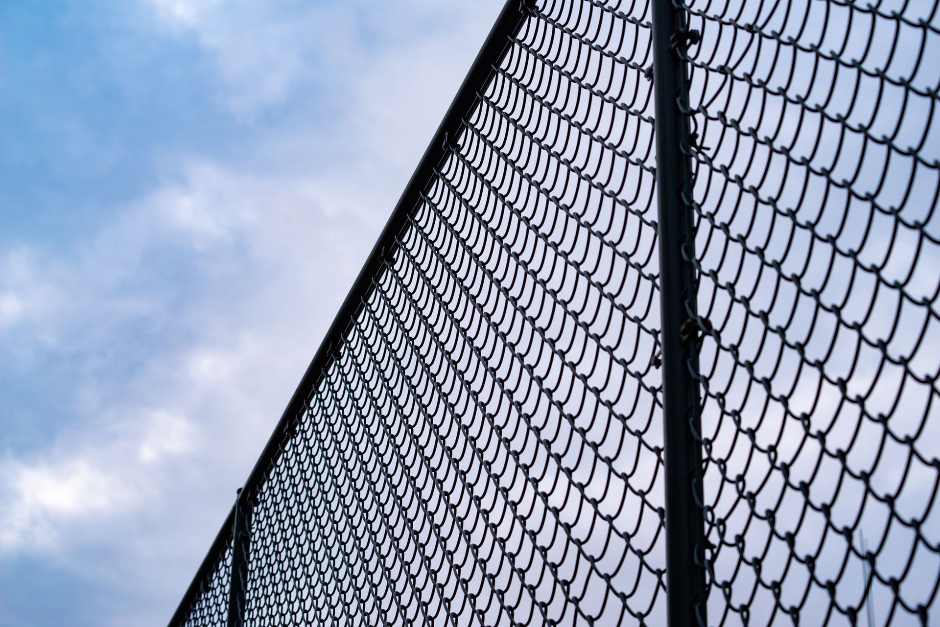 Chain-link fence against a cloudy blue sky.