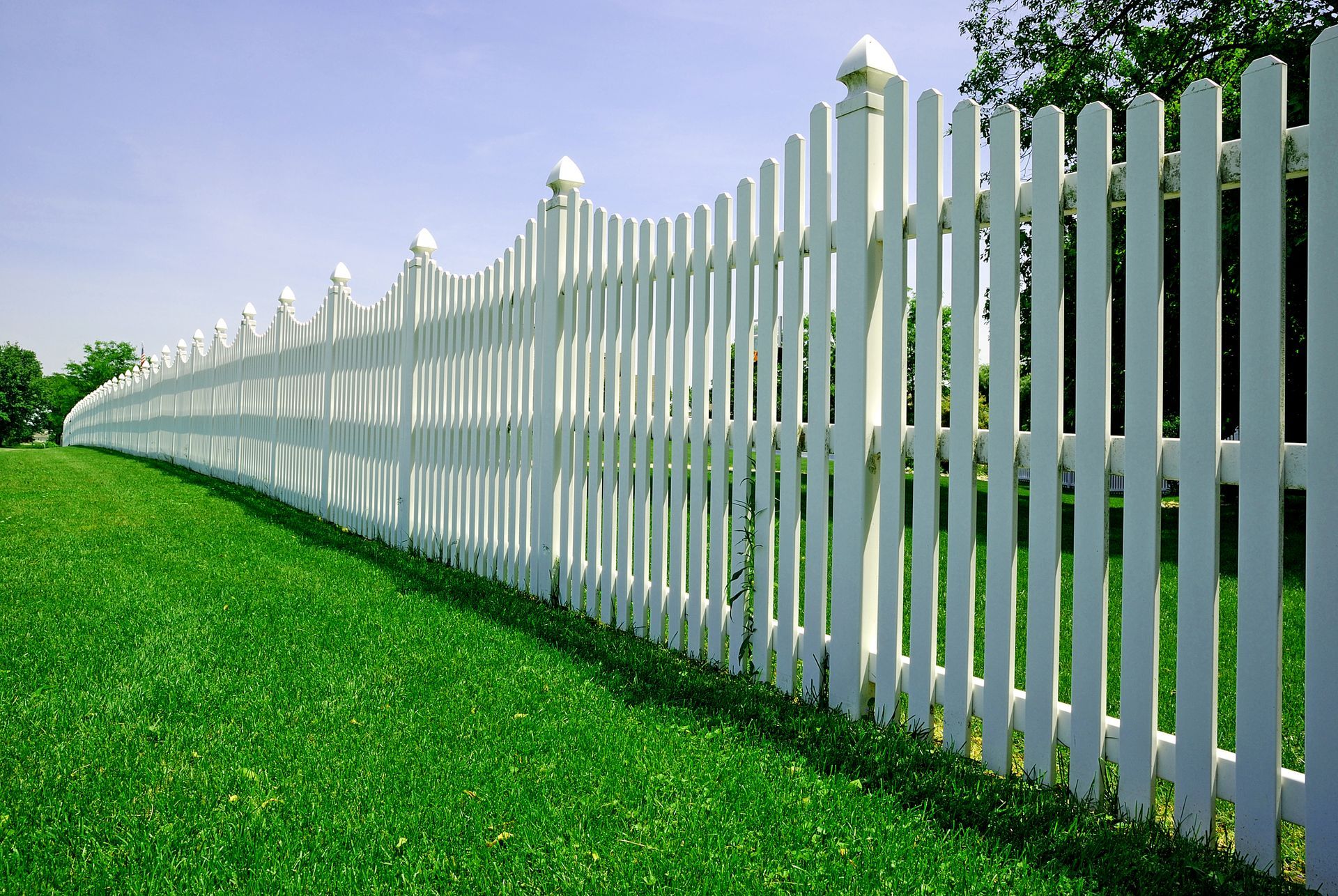 White picket fence on bright green lawn under a blue sky.