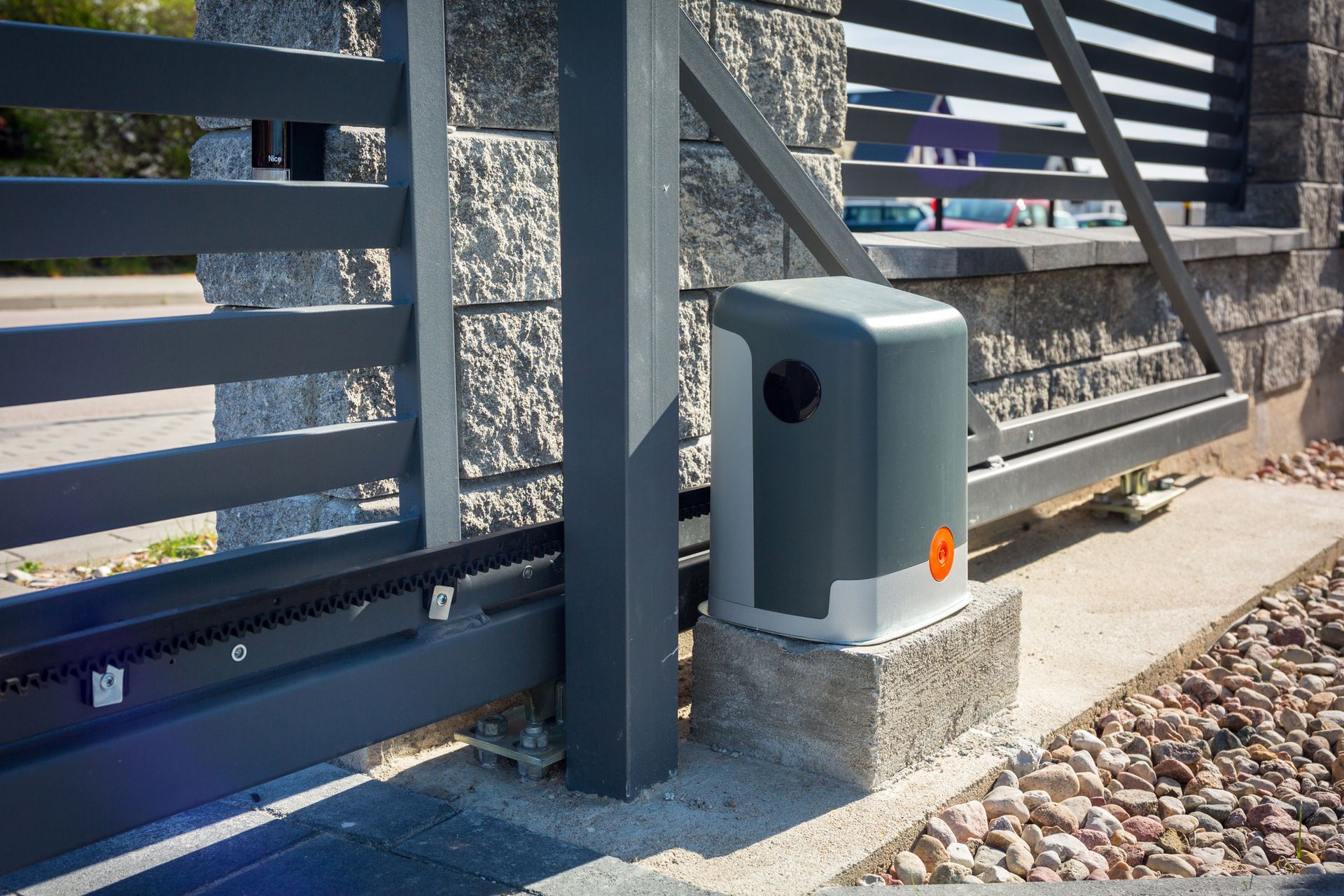 Motorized sliding gate with dark gray frame and automation box on a stone base.
