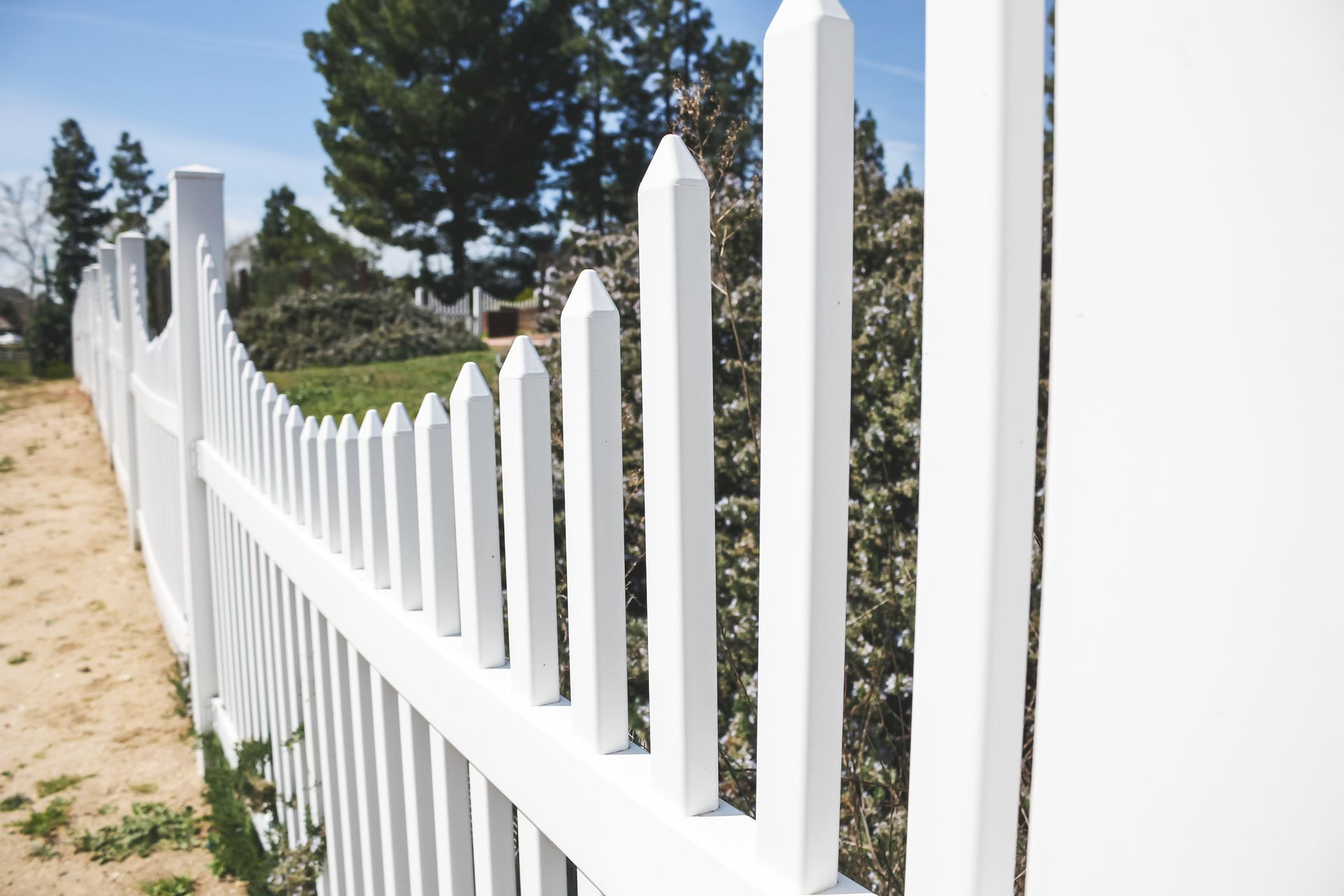 White lattice fence surrounding green grass in front of a house on a sunny day.