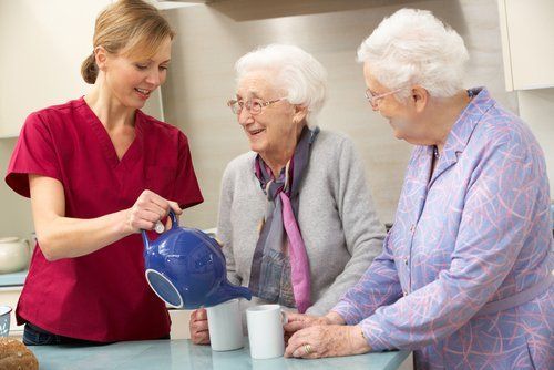 assistente di una casa di riposo versa del tè a due anziani