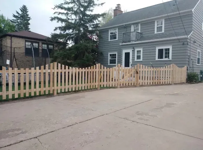 Wooden picket fence in front of a gray two-story house.