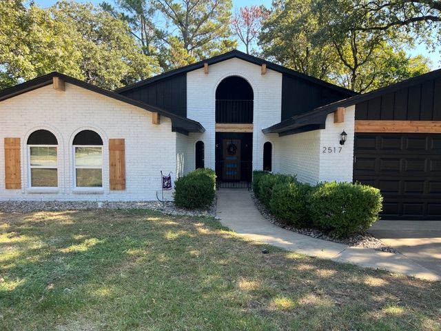 White brick house with black accents, wooden shutters and trim, arched windows and front door, green bushes, and lawn.