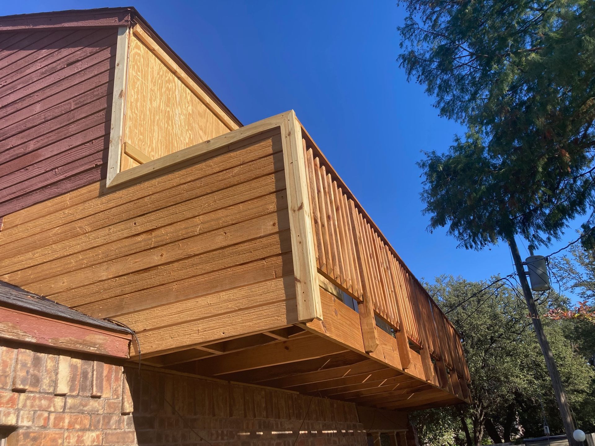 A wooden deck with horizontal siding, attached to a brick building, against a blue sky.