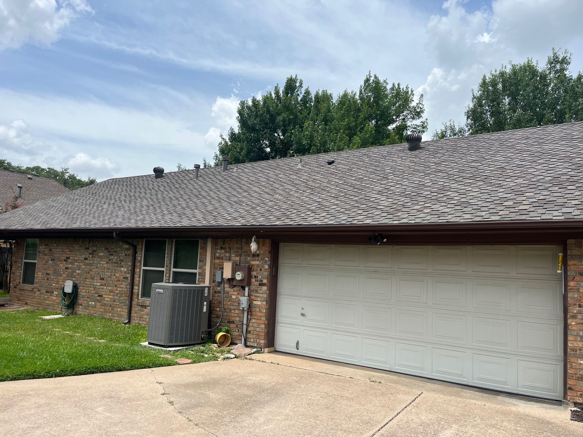 Brick building with a brown roof, white garage door, and air conditioner. Overcast sky.