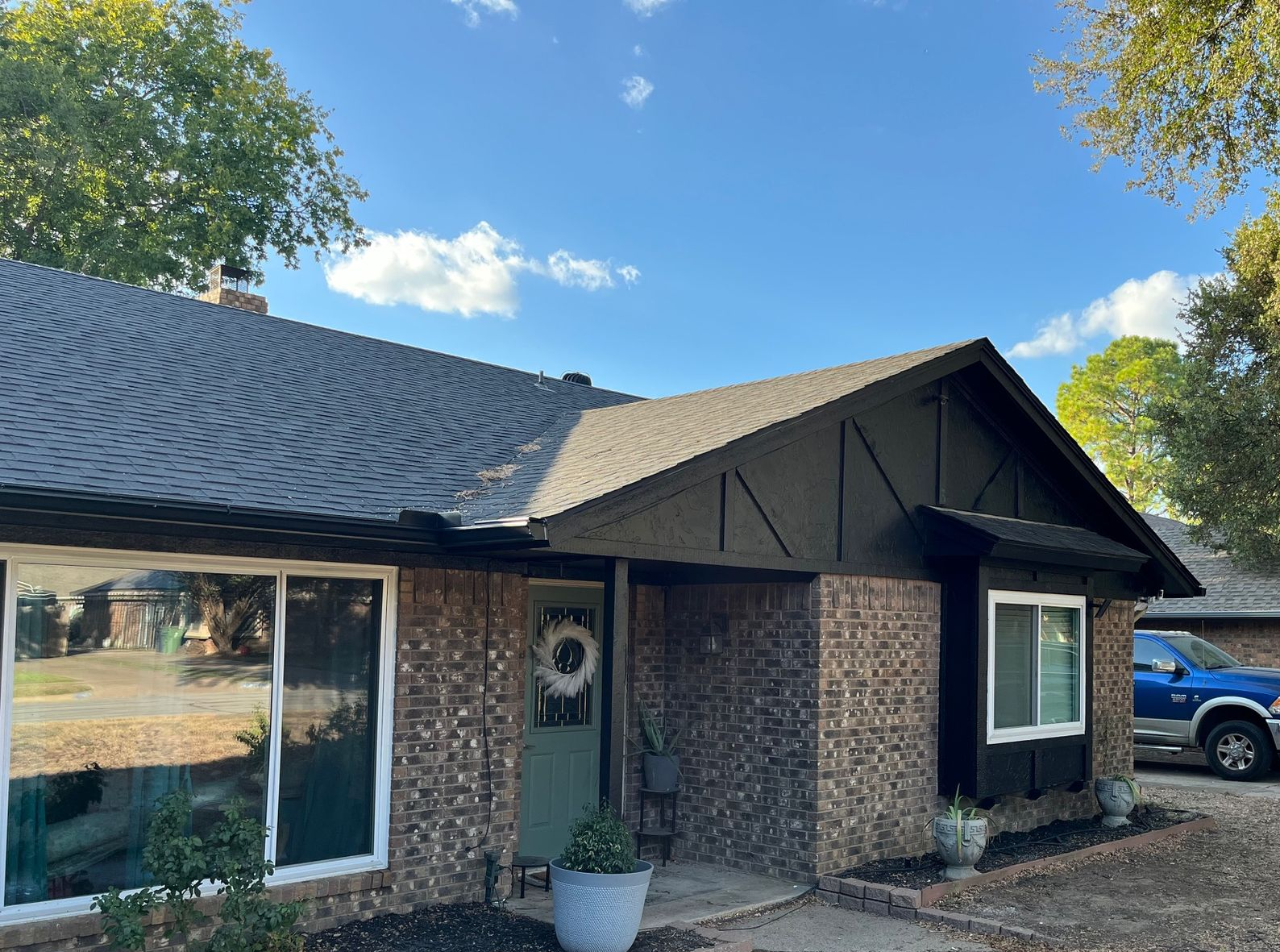 Brick house with dark roof, door, and trim. Blue sky.