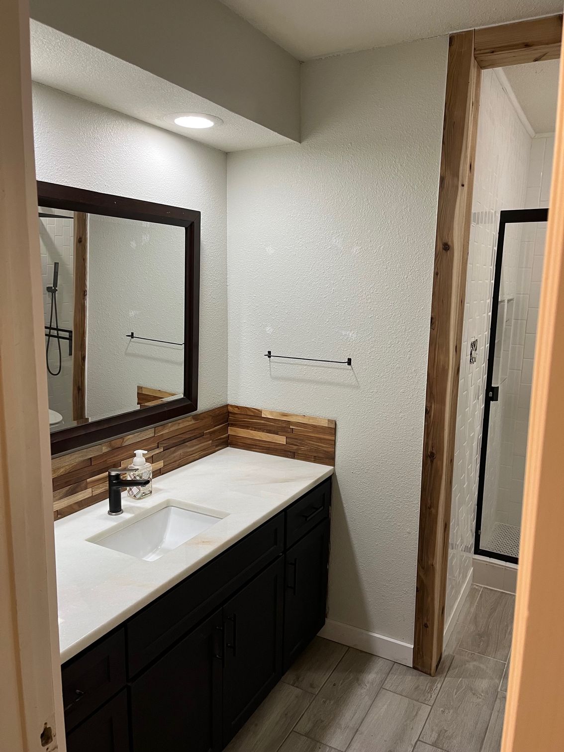 Bathroom with dark vanity, white countertop, wood accents, and a shower.