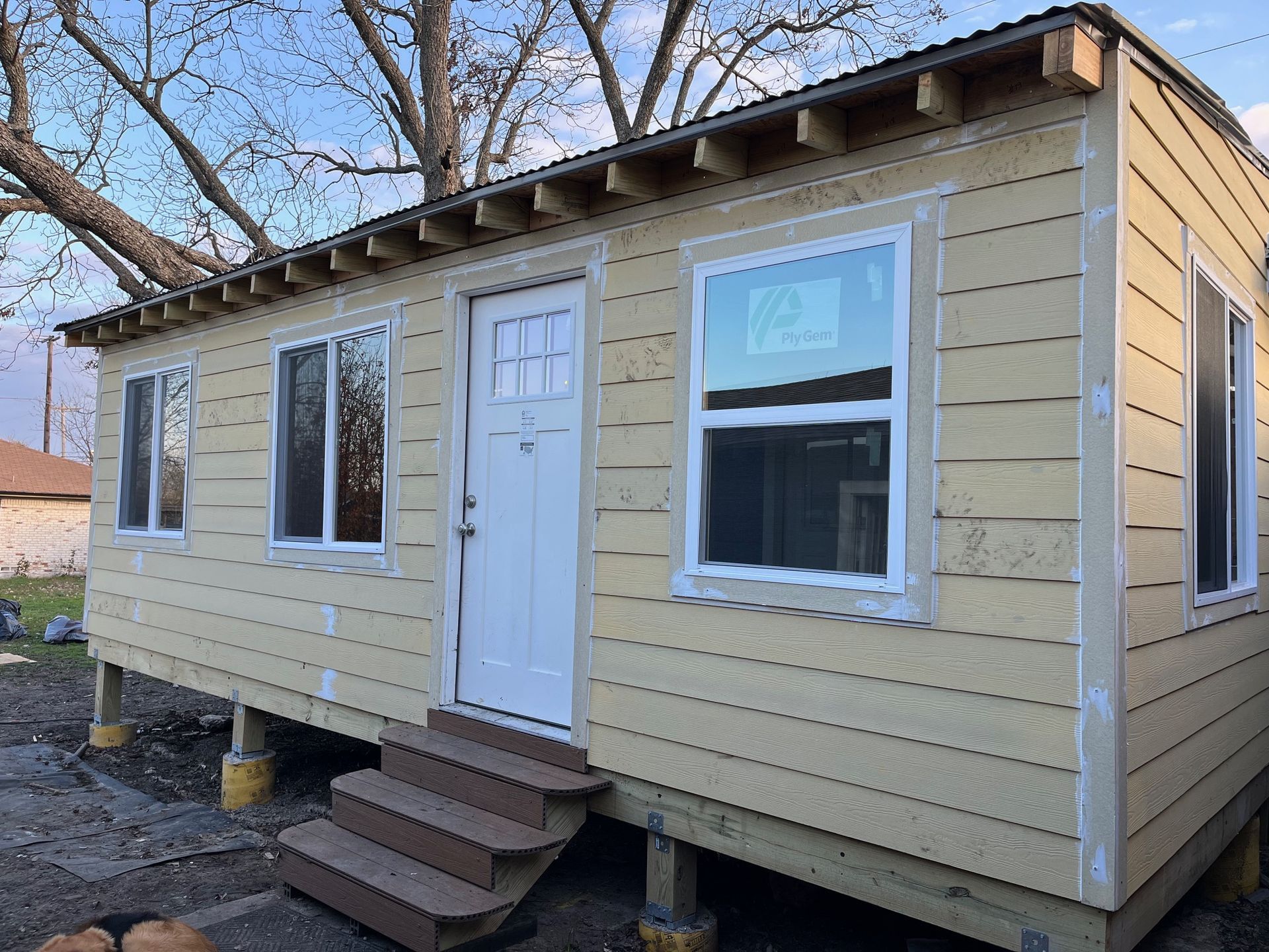 Small yellow building with white trim and door, windows, and steps.  It sits on concrete supports.