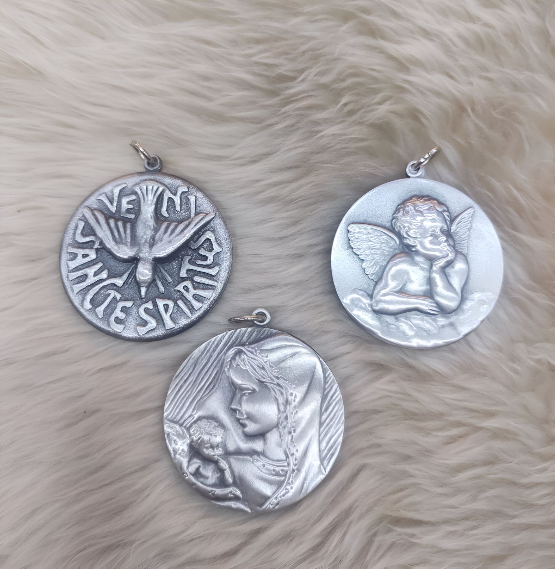 Tres colgantes religiosos de plata se encuentran sobre una superficie peluda.