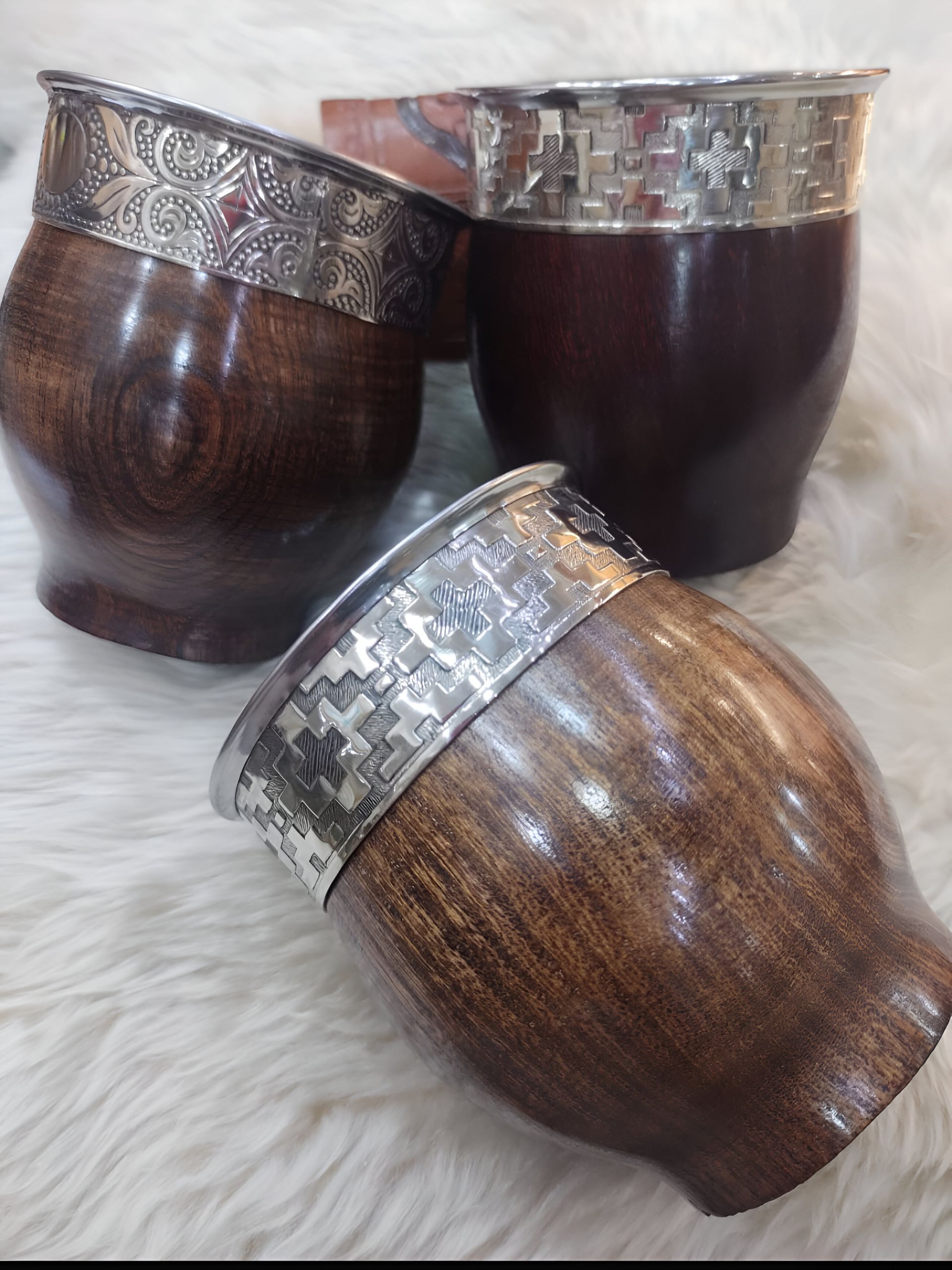 Tres mates de madera con adornos plateados se encuentran sobre una superficie peluda.