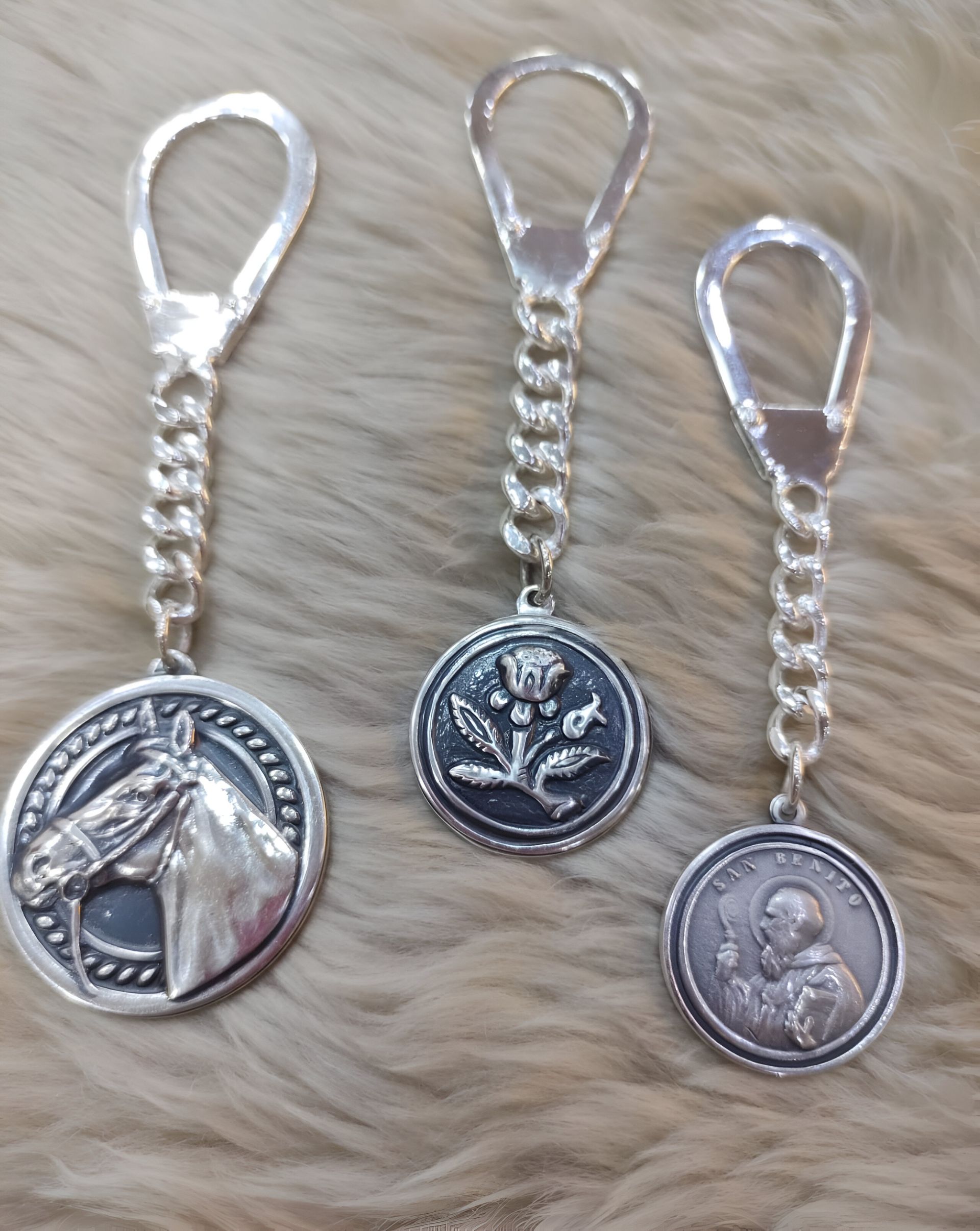 Tres llaveros de plata con caballos y flores.
