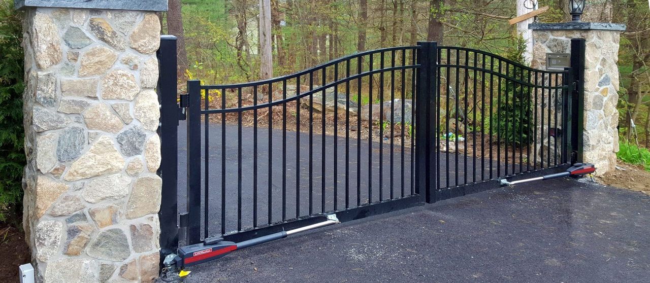 A black wrought iron gate is sitting on the side of a road next to a stone wall.
