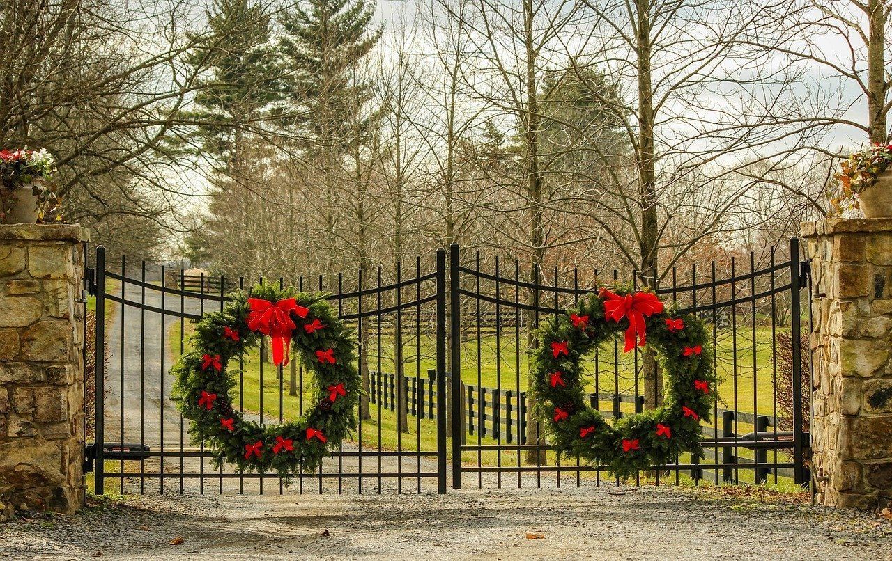 A wrought iron gate decorated with christmas wreaths and a red bow.