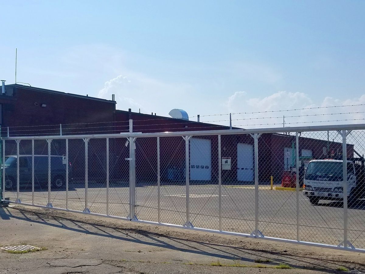A chain link fence surrounds a parking lot with a brick building in the background.