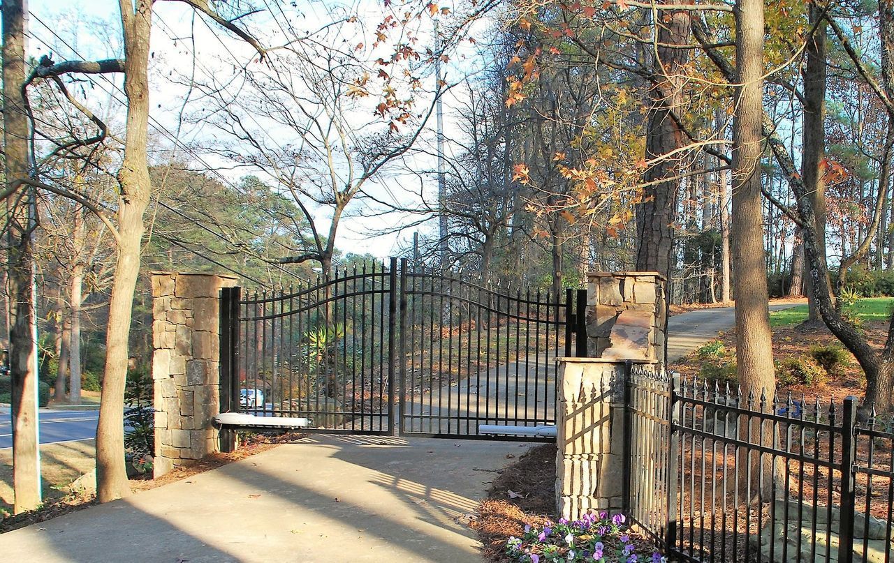 A black wrought iron gate is surrounded by trees and flowers.