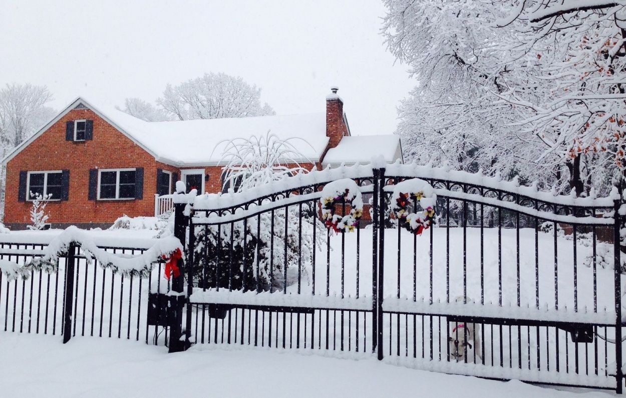 A fence is covered in snow in front of a brick house.