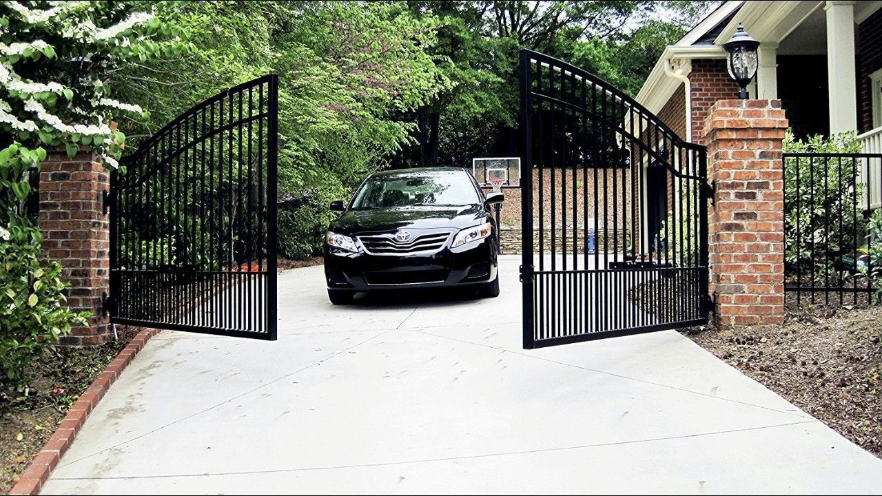 A black car is parked in a driveway next to an open gate.