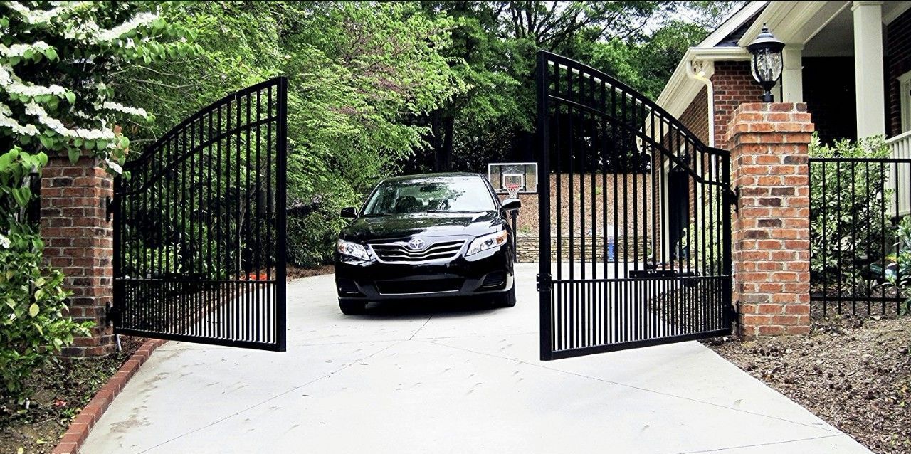 A black car is parked in a driveway next to a wrought iron gate.