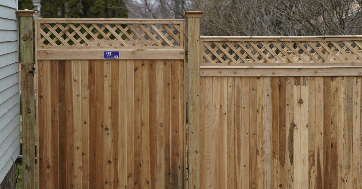 Wooden backyard fence with lattice top panels beside a white house, with bare trees in the background