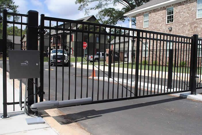 Black metal security gate at an entrance to a residential area. A car is visible on the street.