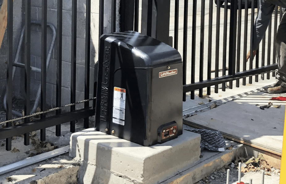 Black automatic gate opener mounted on a concrete base next to a metal gate.