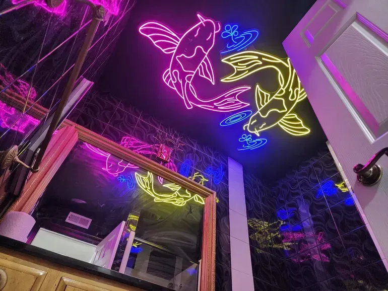 A bathroom with a neon sign of two fish on the ceiling.